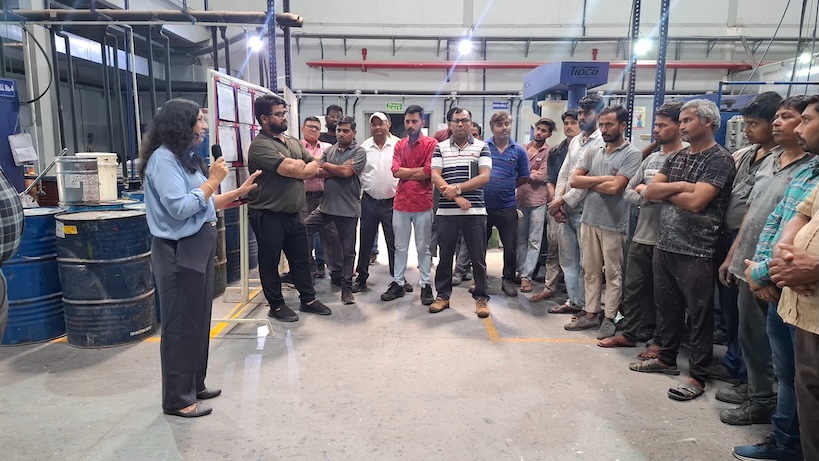 A woman addressing a group of workers inside an industrial facility