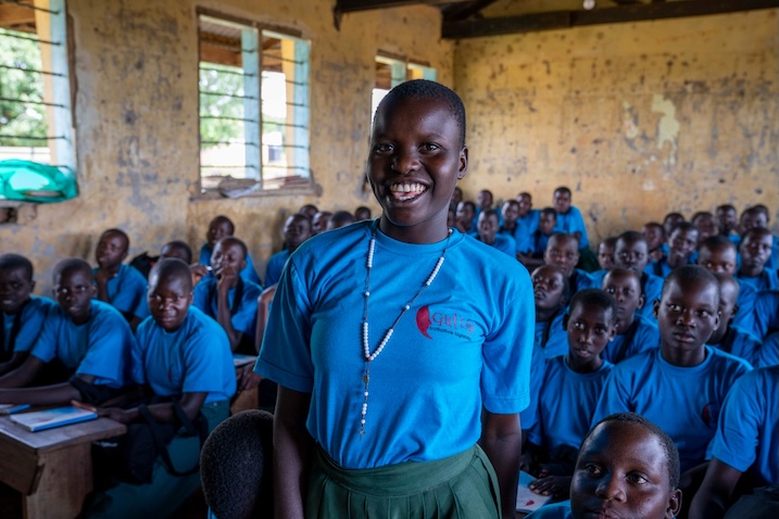 Young participant standing in front of classmates wearing blue Girl Up Initiative Uganda shirts.
