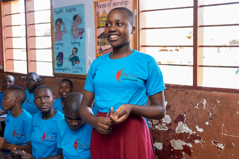 Student in a blue Girl Up Initiative Uganda shirt standing and speaking in a classroom.