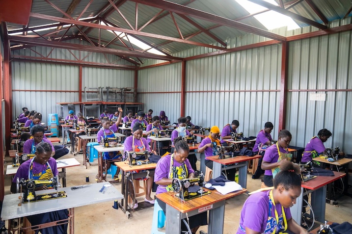 Young women in purple shirts seated at sewing machines in a training workshop.