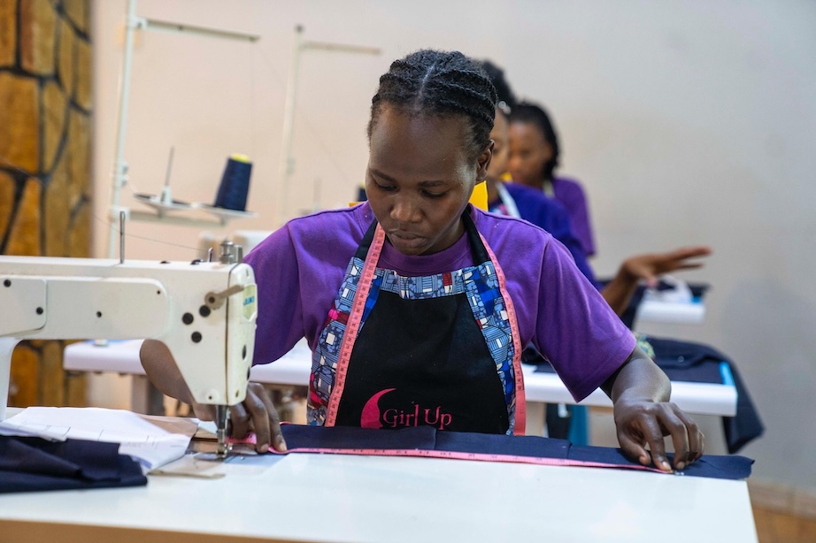 Young woman in a purple shirt and measuring tape working at a sewing machine.
