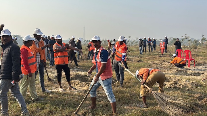 Field workers in safety vests clear vegetation with hand tools.
