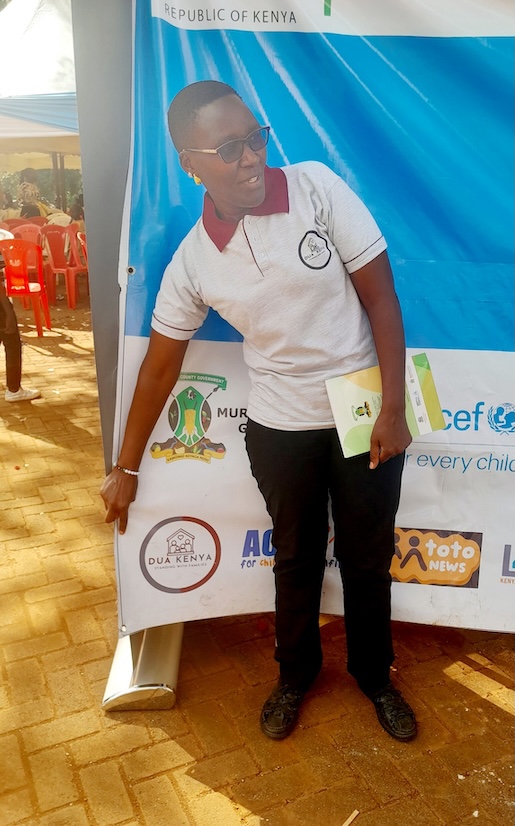 An adult standing beside an event banner and display materials.