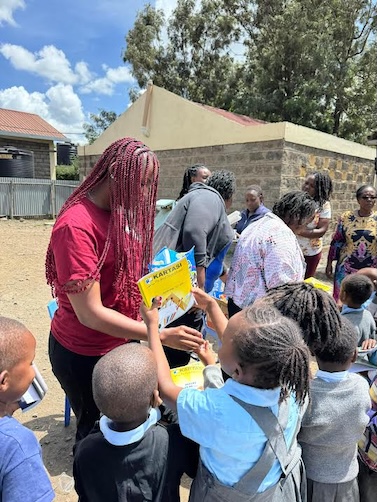 An adult distributing learning materials to children outdoors.