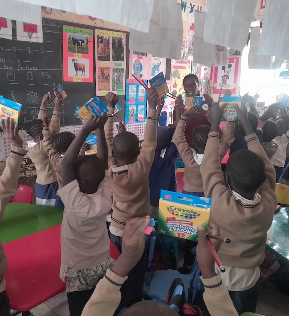 Children in a classroom raising colourful learning materials.
