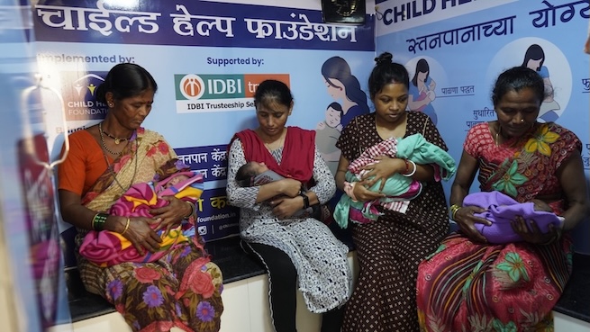 Four women sit beside one another holding and feeding their infants.